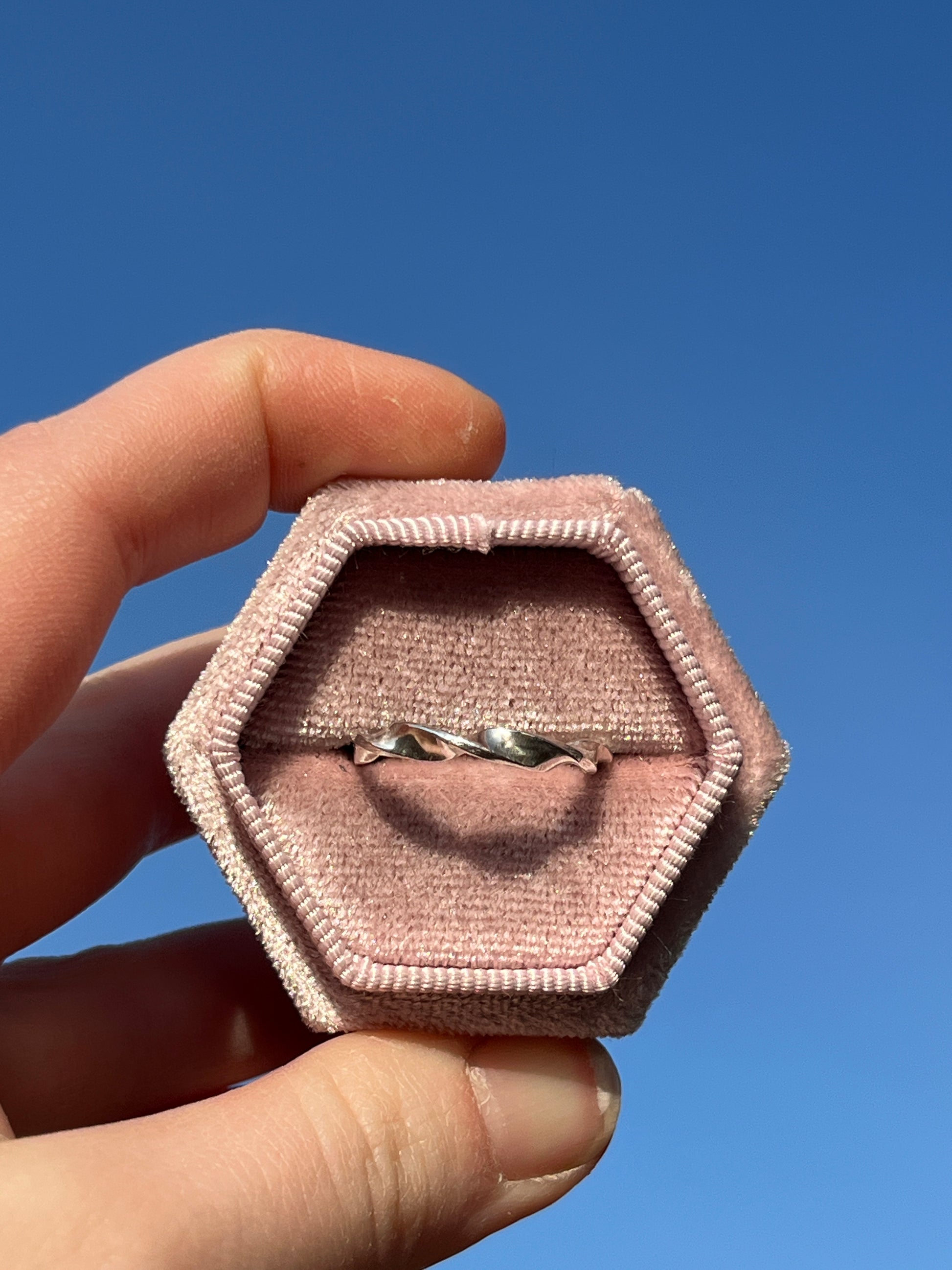 Helix ring pictured against blue sky in a pink ring box