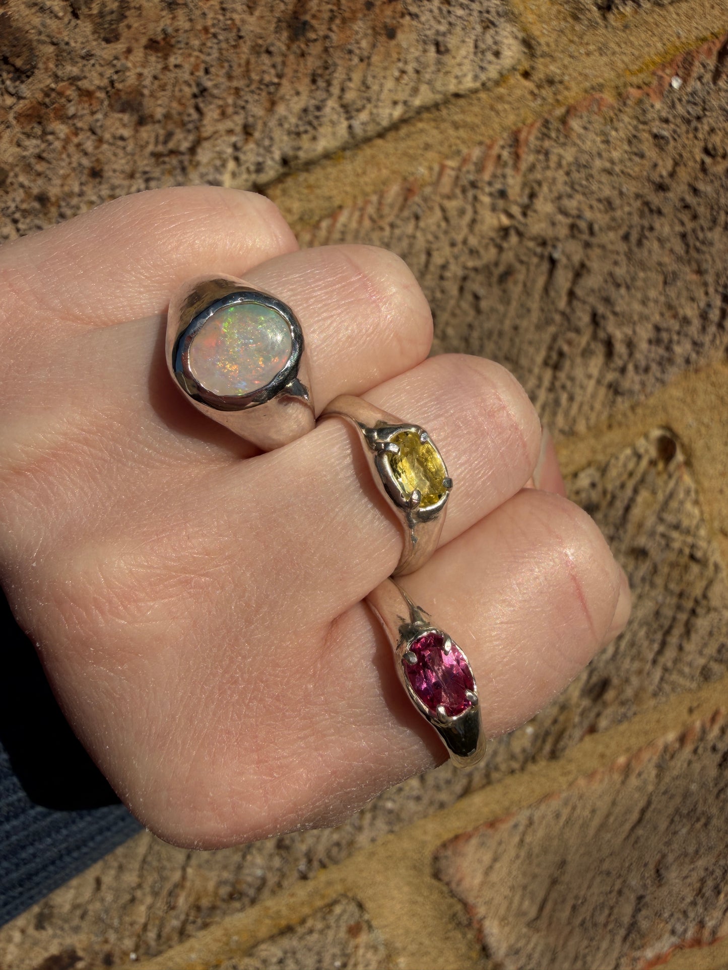 Hand wearing three rings with different gemstones on a textured surface