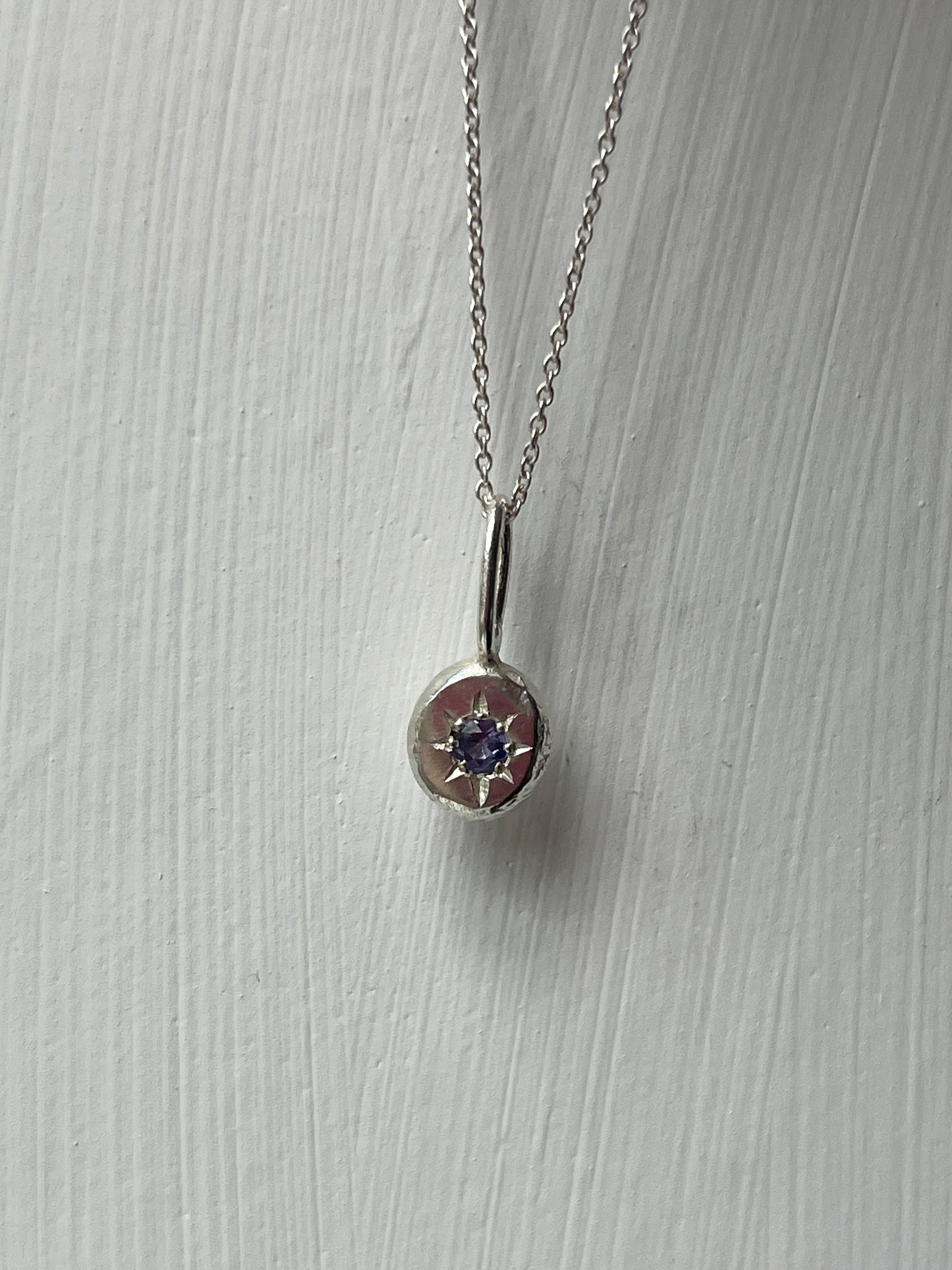 a sterling silver pendant with a star set tanzanite gemstone on a silver trace chain, pictured against a white background.