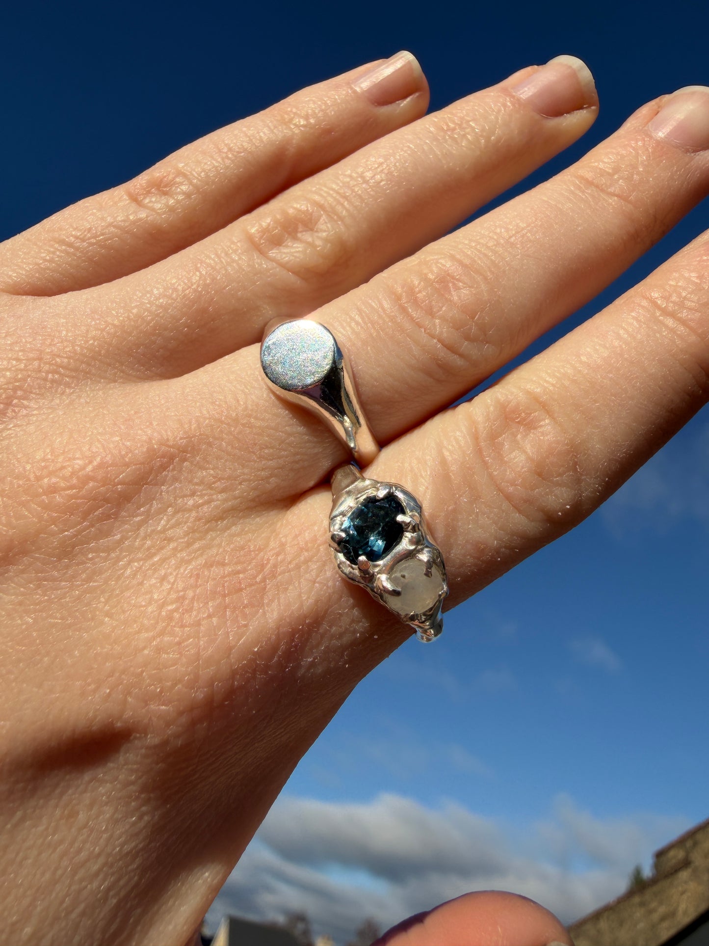 The silver mini signet pictured on a hand against a blue sky backgorund