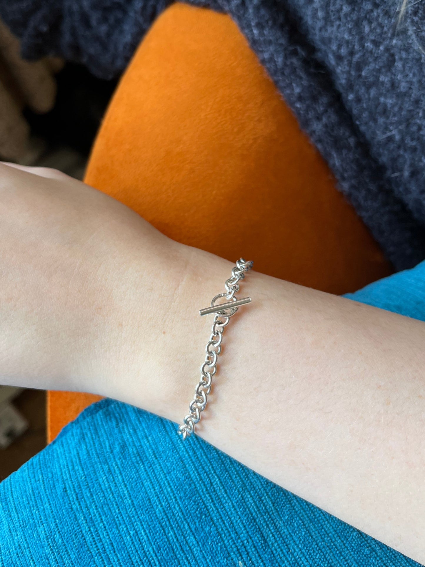 sterling silver chain with round links and a t-bar clasp, shown worn on a model. pictured against blue and orange upholstery