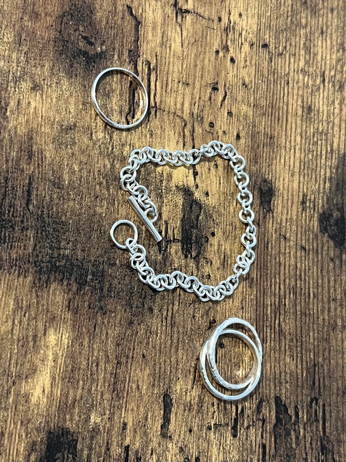 nova chain pictured flat against oak. sterling silver bracelet with round links and t-bar clasp. Pictured with 2 rings, one plain silver stackers and the moon rock ring