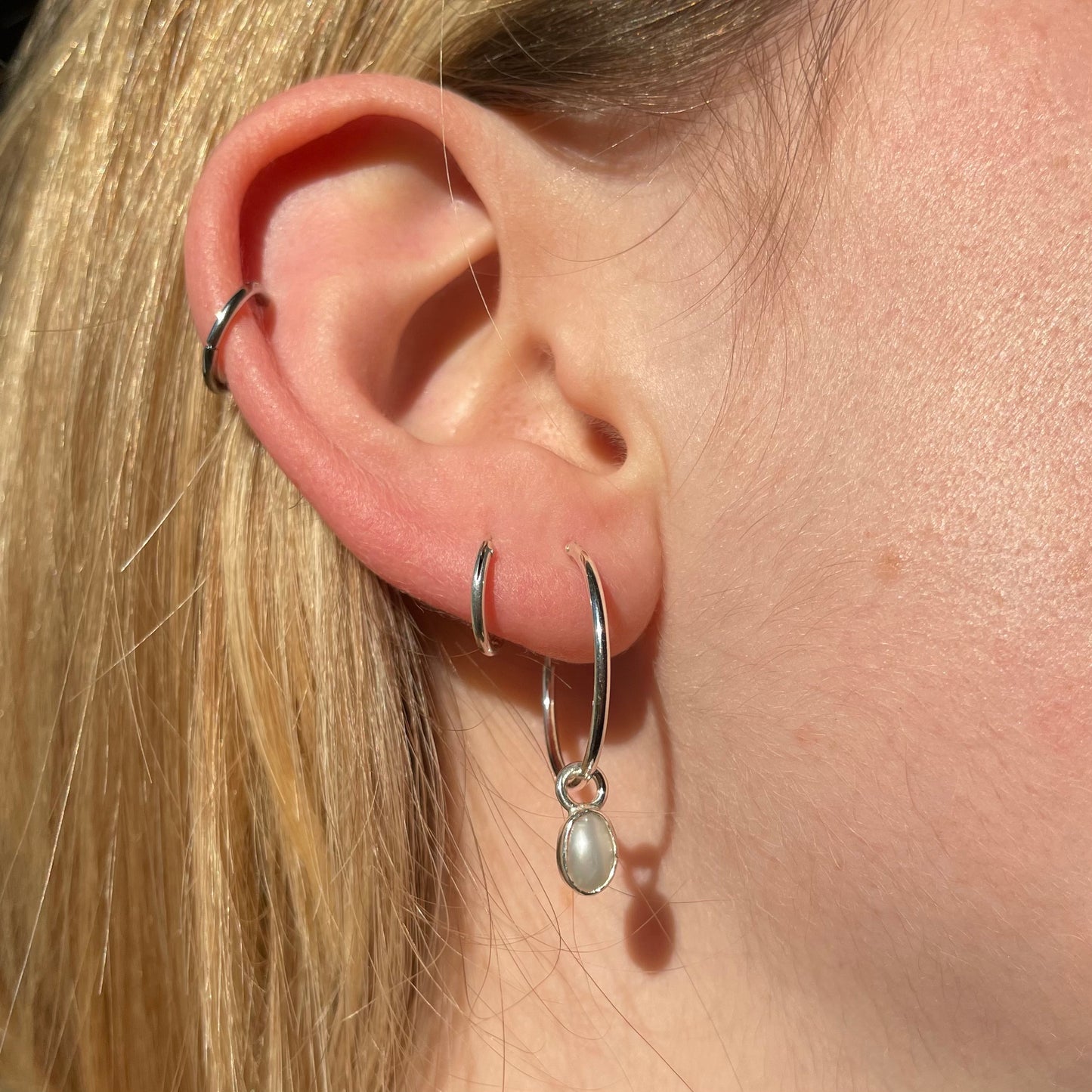 pearl droplet earring with sterling silver bezel on a sterling silver hoop 20mm wide. pictured modelled in ear.