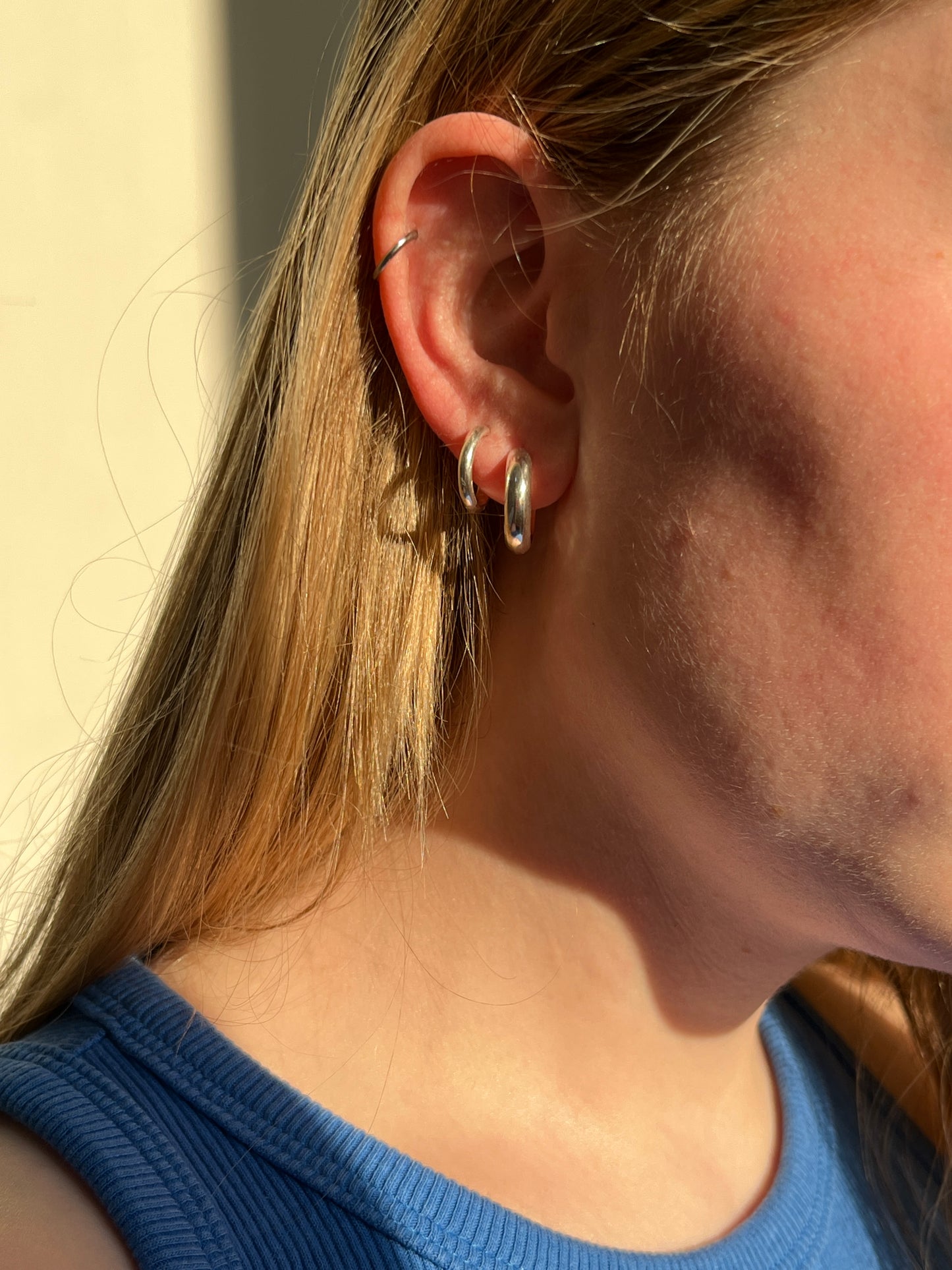 Close-up of an ear with the simple hoop earrings styled in a stack, on a girl wearing a blue top.