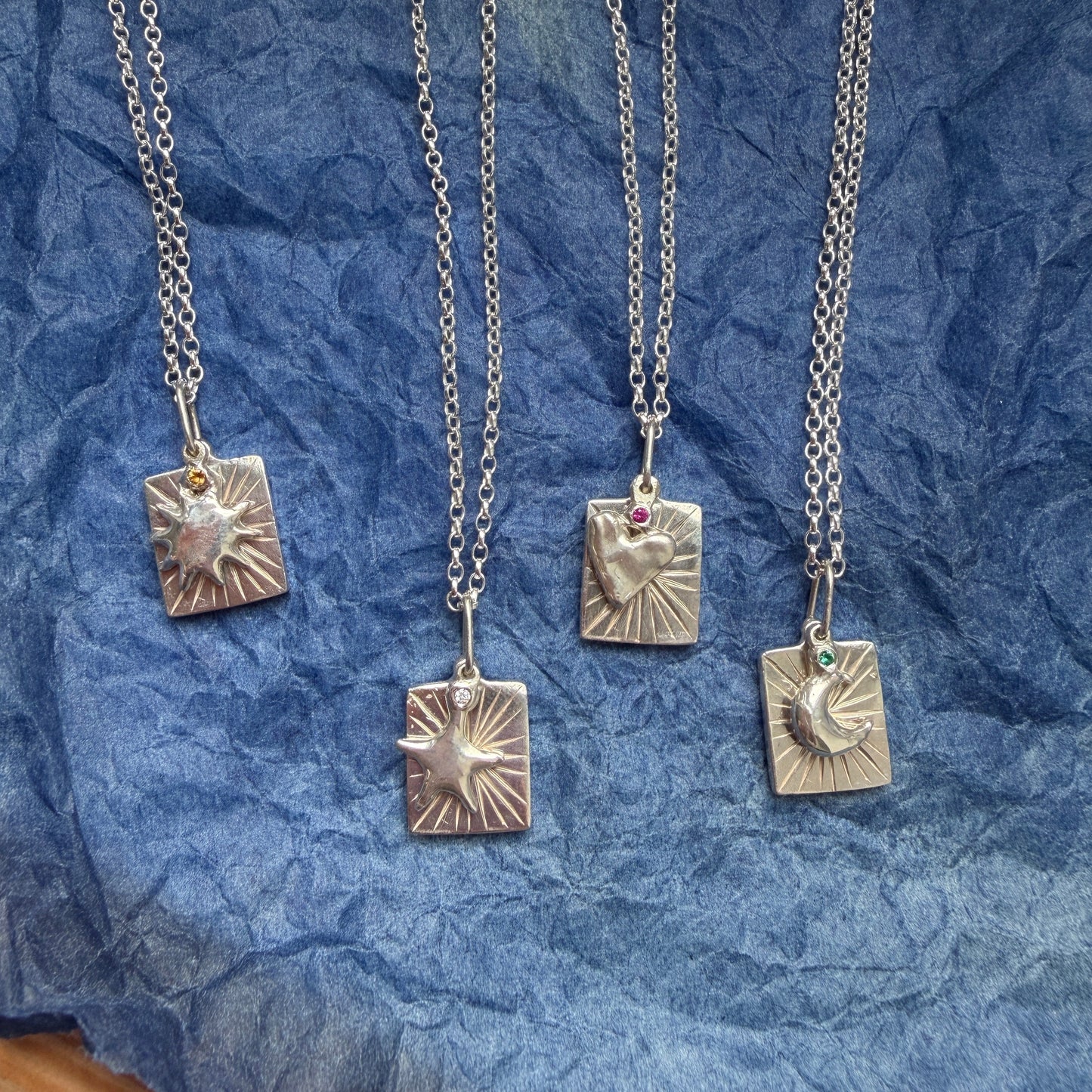 Silver necklaces with charm pendants on a blue textured surface