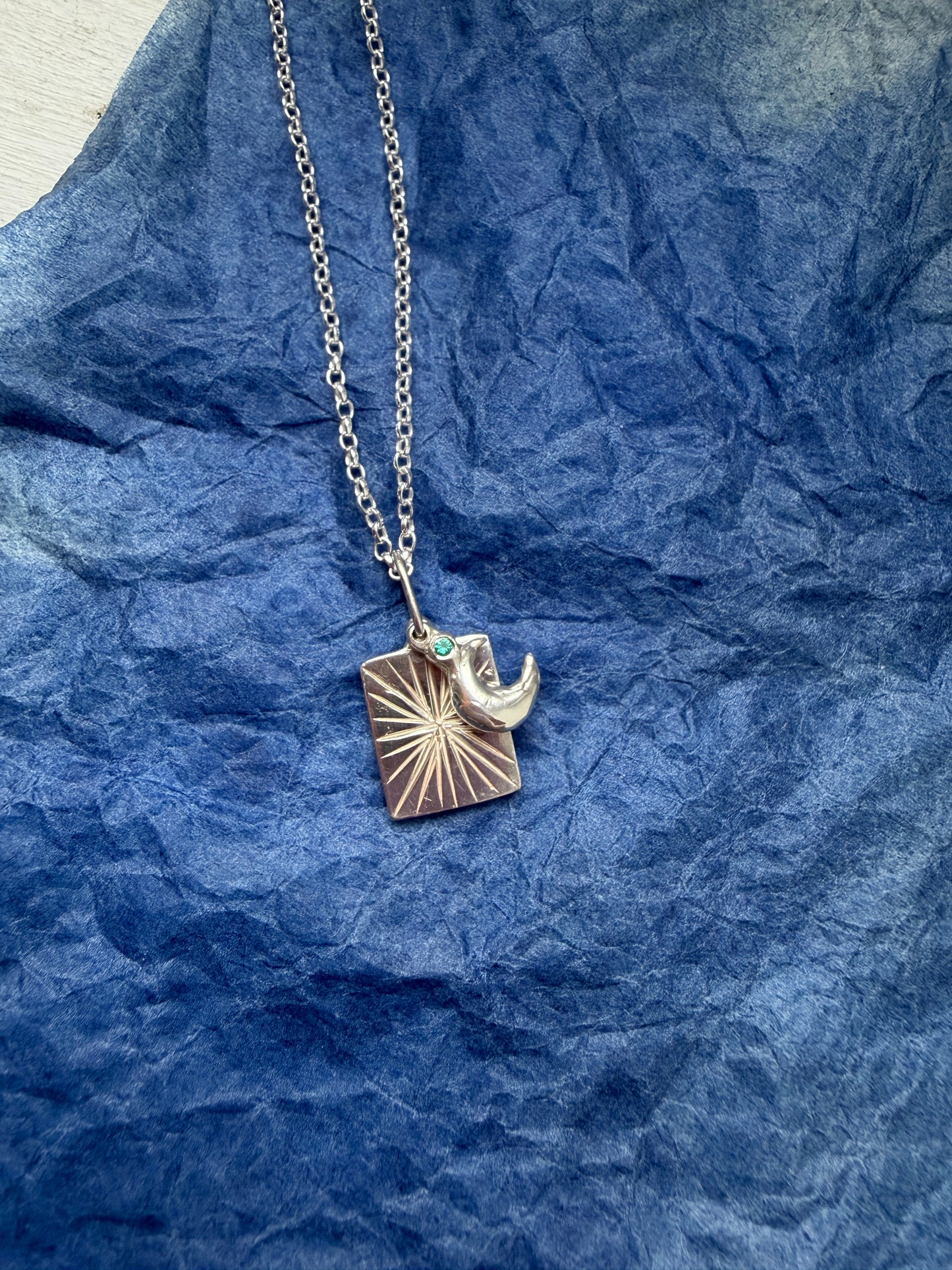 Silver necklace with a moon pendant on blue textured fabric