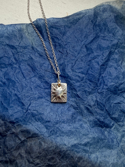 Silver necklace with a sun shaped pendant on a blue textured background