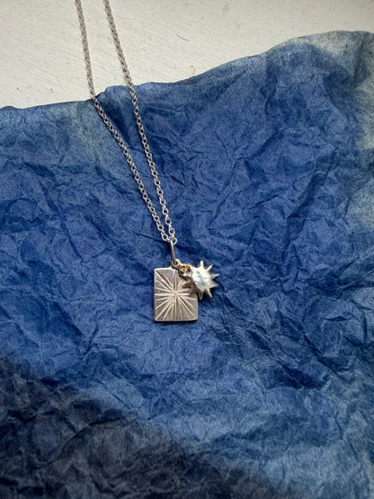 Silver necklace with a sun pendant on a blue textured background