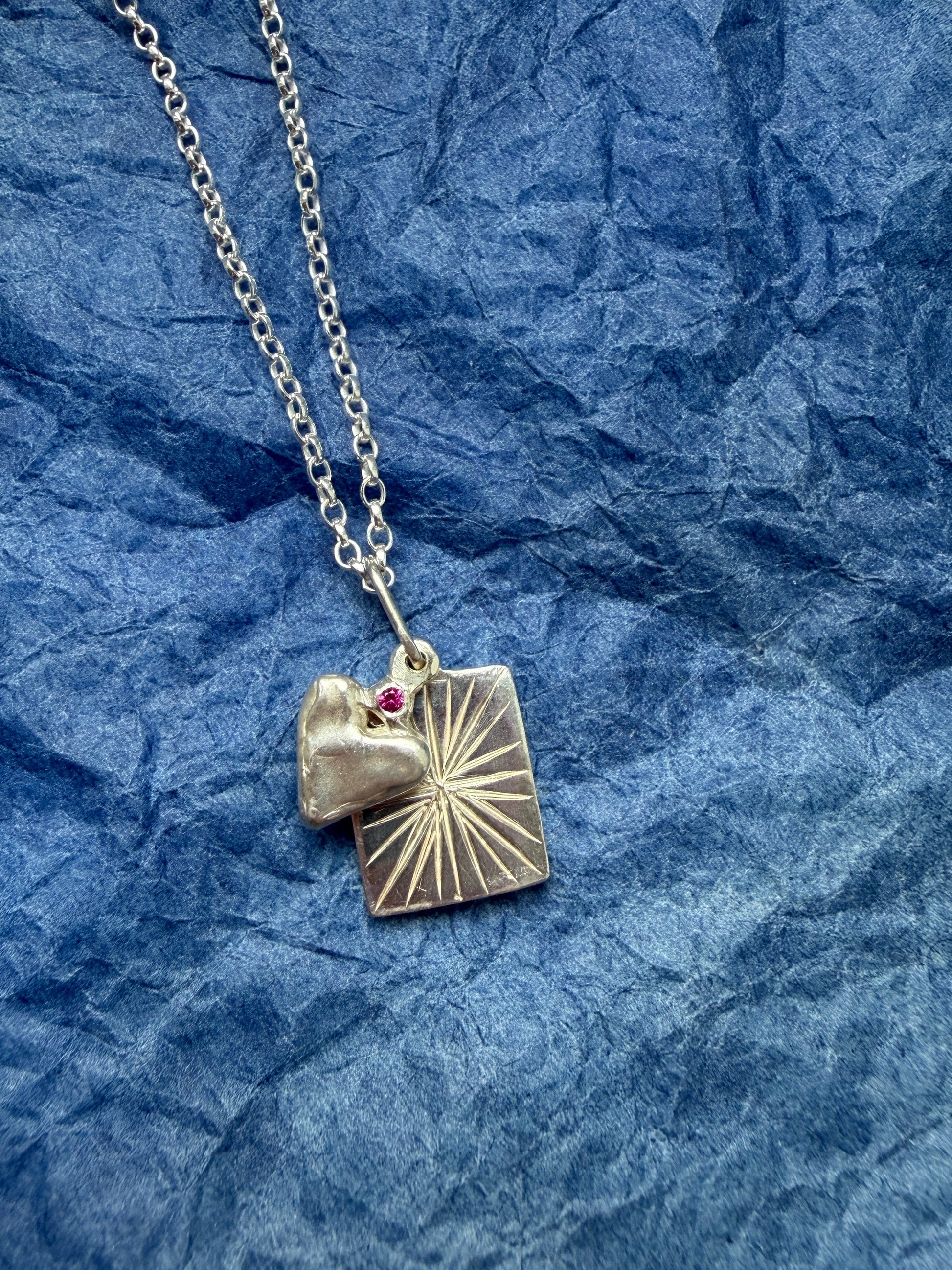 Silver necklace with a heart pendant with a ruby gem on a blue textured background