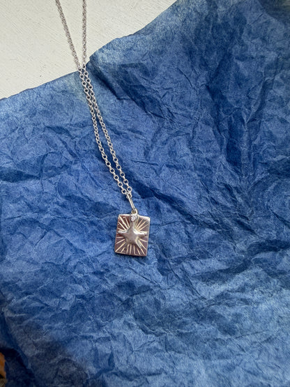 Silver necklace with a star pendant on a blue textured surface