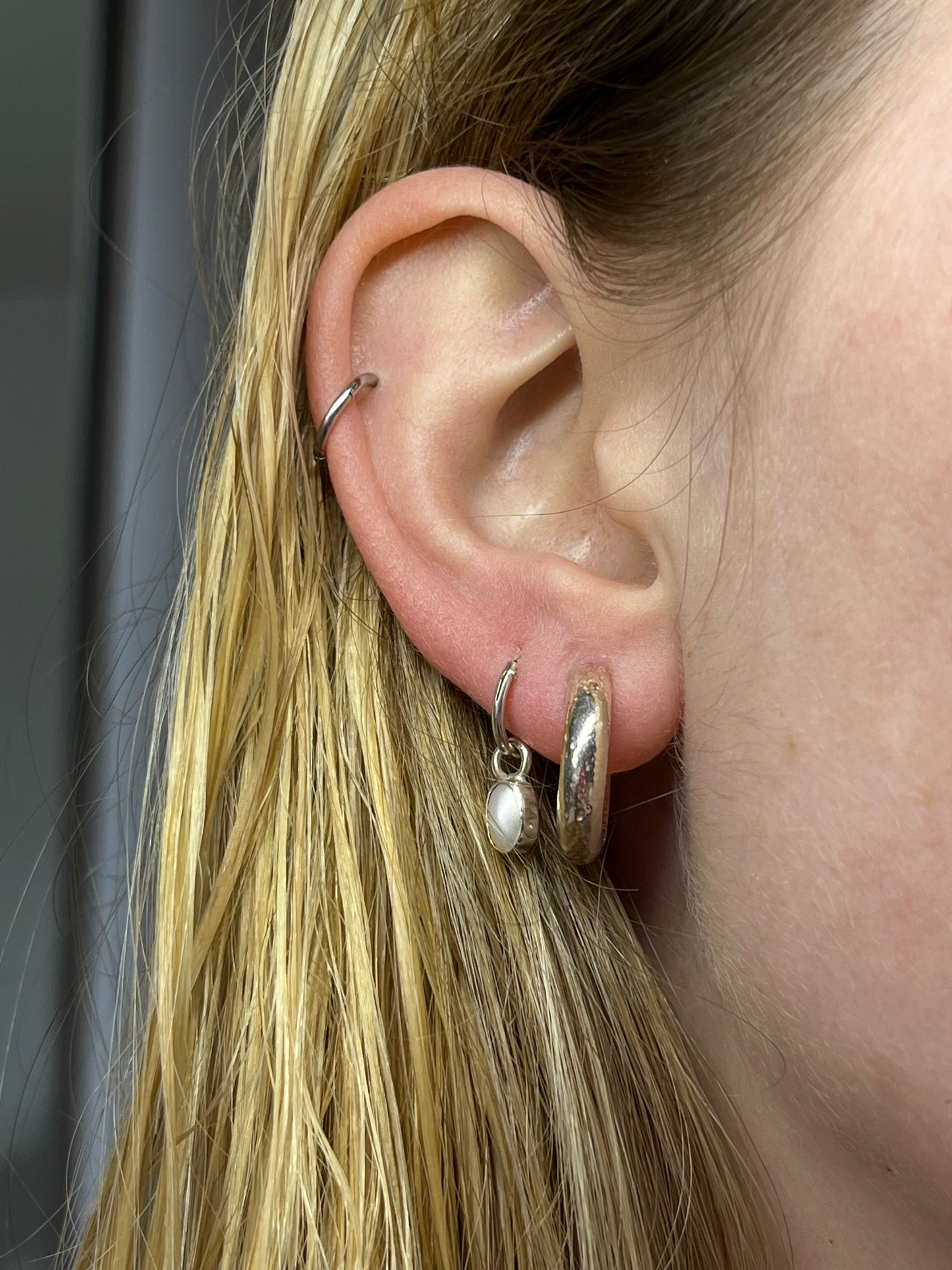 crater hoops pictured in ear paired with pearl droplets. sterling silver hoops with molten texture