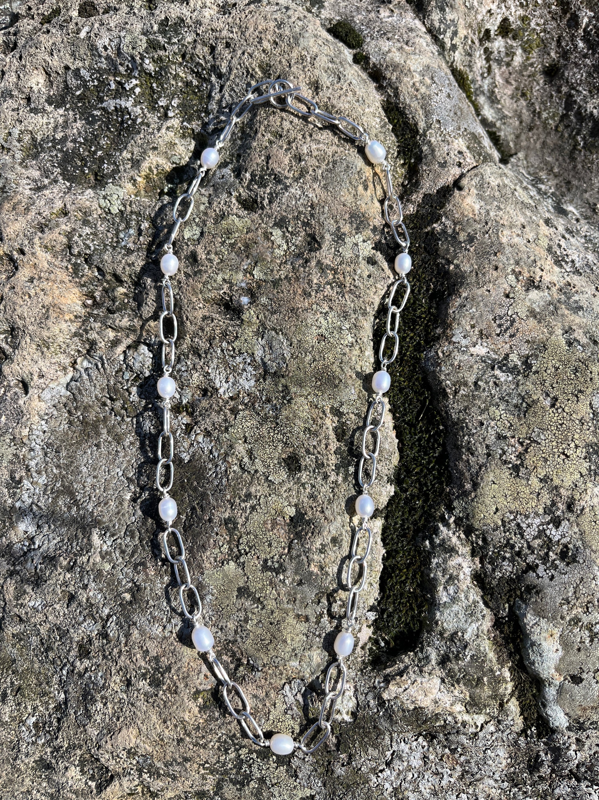Handmade silver chain necklace with white, freshwater pearls and a t-bar clasp, pictured on a stone surface