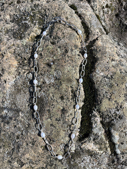 Handmade silver chain necklace with white, freshwater pearls and a t-bar clasp, pictured on a stone surface
