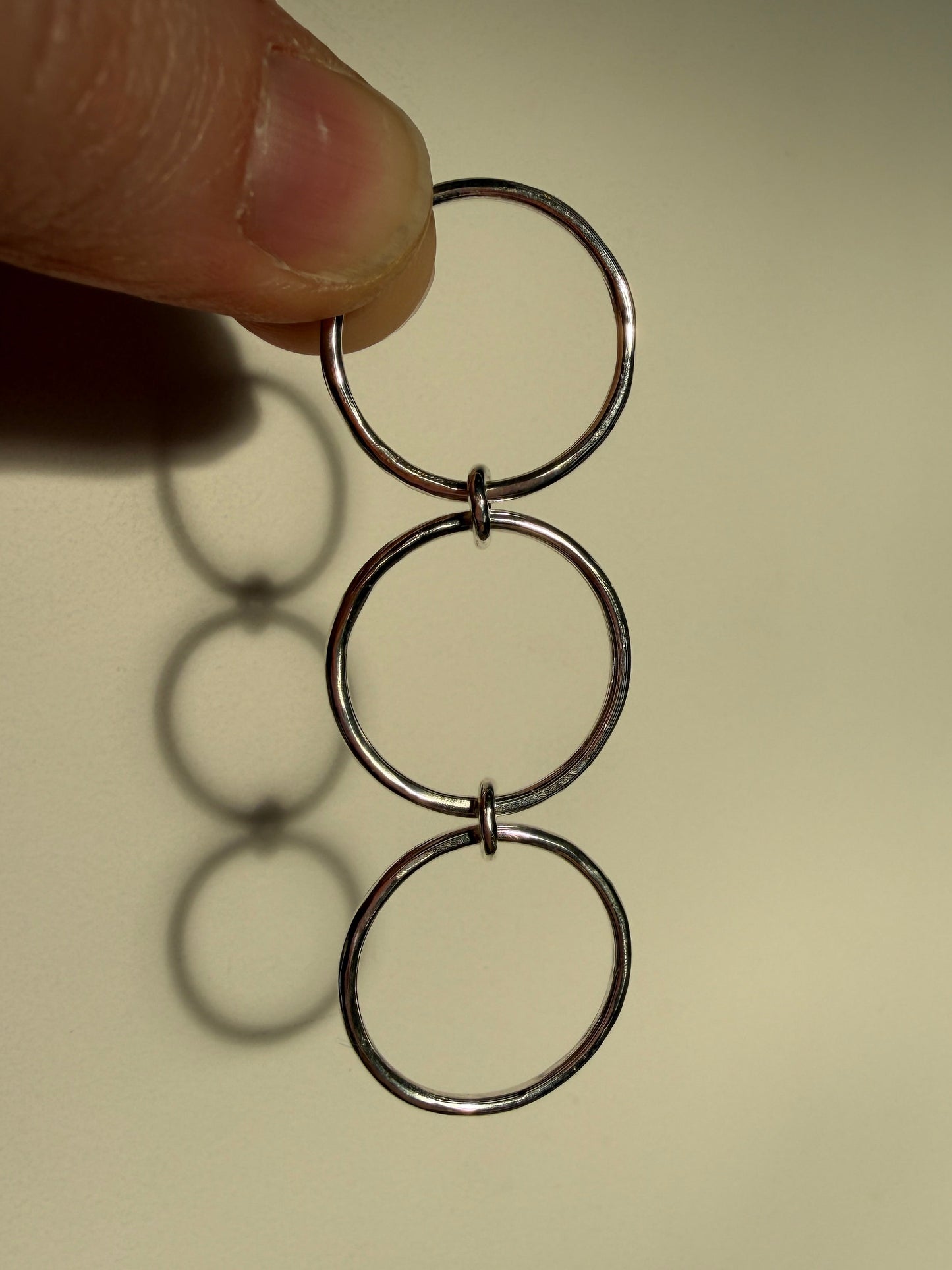 A sterling silver ring made up of 3 bands linked by 3 small jumprings, hanging down showing composition. pictured against cream background.
