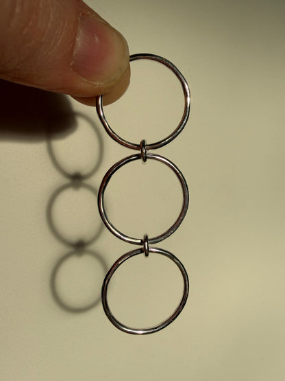 A sterling silver ring made up of 3 bands linked by 3 small jumprings, hanging down showing composition. pictured against cream background.