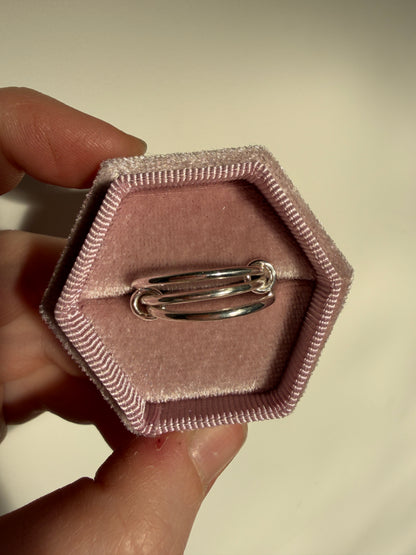 A sterling silver ring made up of 3 bands linked by small jumprings, pictured in a pink velvet box.