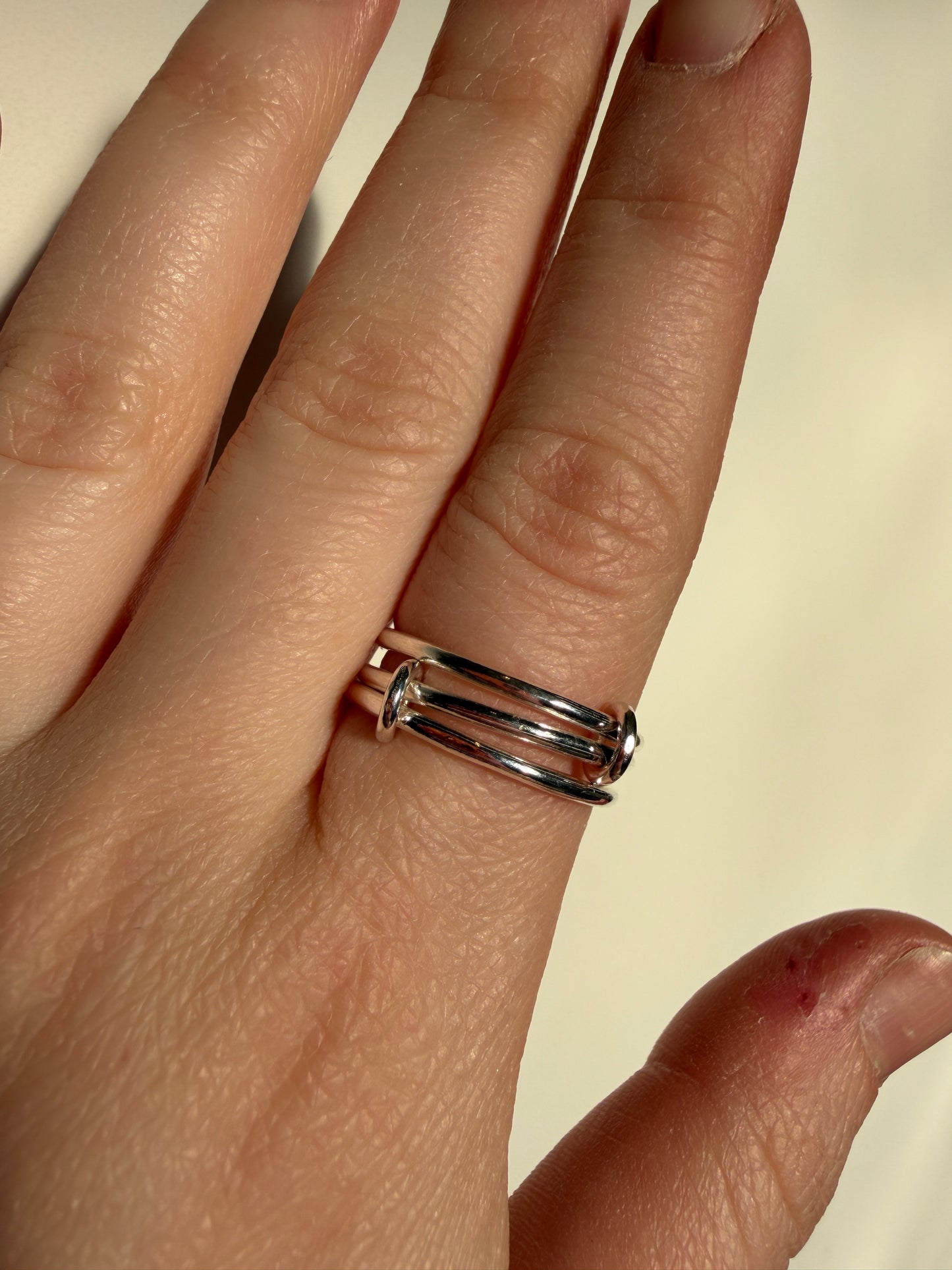 A sterling silver ring made up of 3 bands linked by small jumprings, pictured worn on a hand.