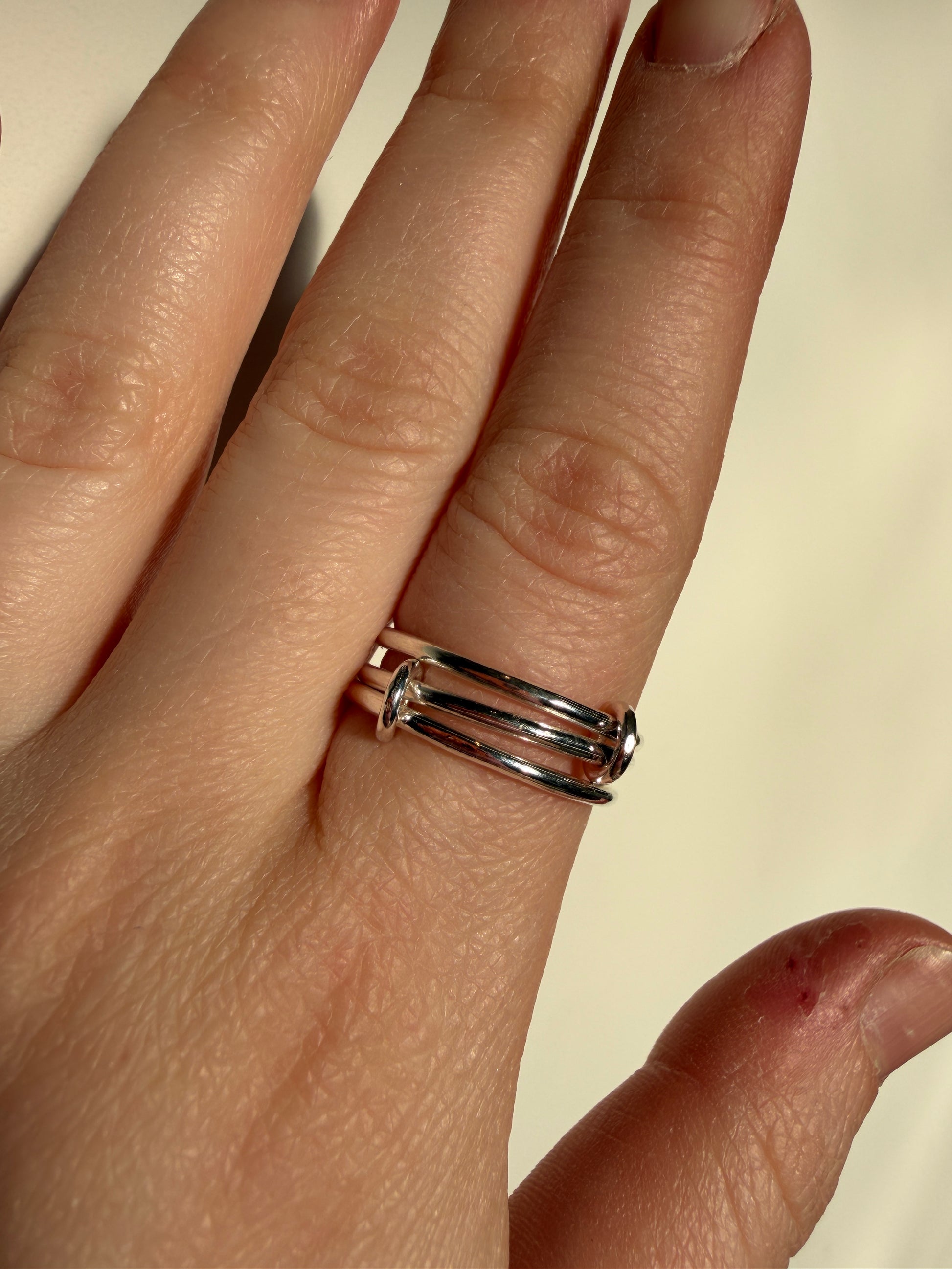 A sterling silver ring made up of 3 bands linked by small jumprings, pictured worn on a hand.