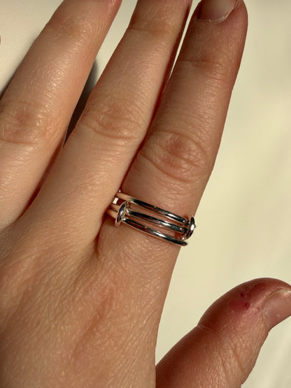 A sterling silver ring made up of 3 bands linked by small jumprings, pictured worn on a hand.