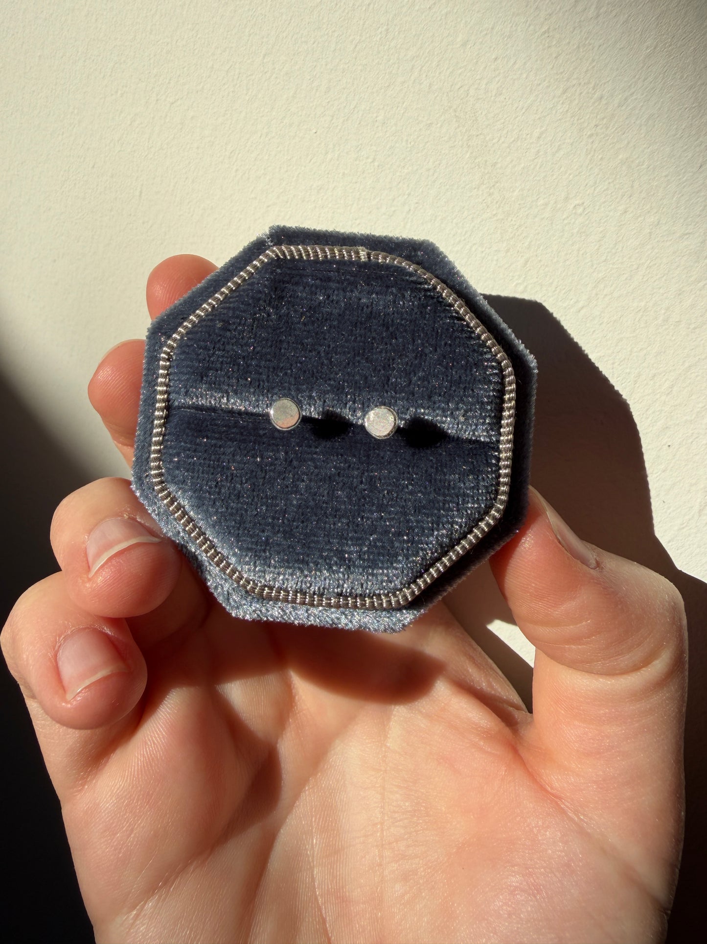recycled silver studs in a blue velvet box held infront of a white wall