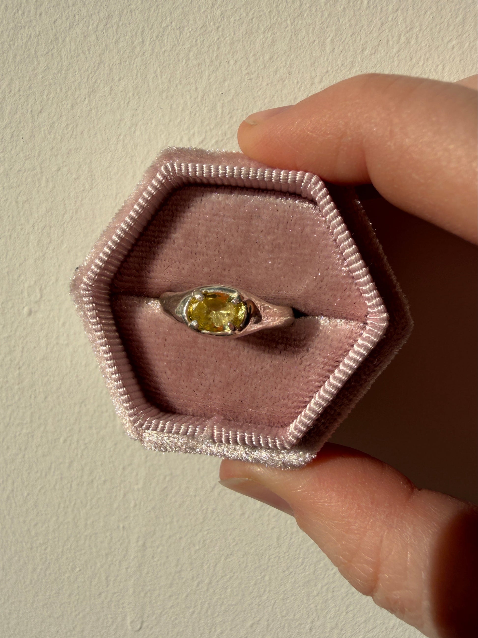 Ring with a yellow gemstone in a hexagonal pink box held by a hand.