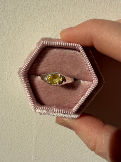 Ring with a yellow gemstone in a hexagonal pink box held by a hand.