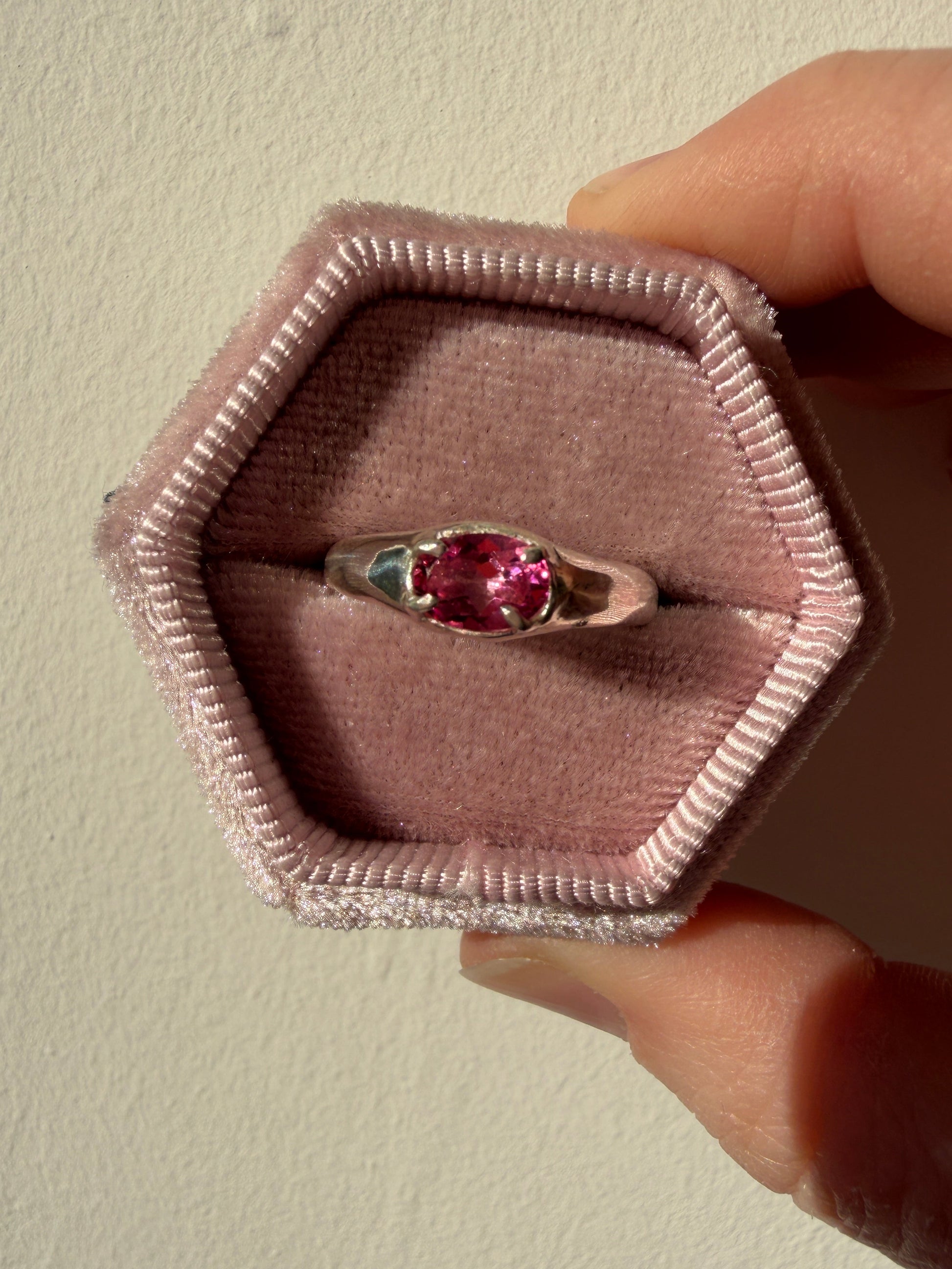 Silver ring with a pink gemstone in a hexagonal pink box held by a hand.