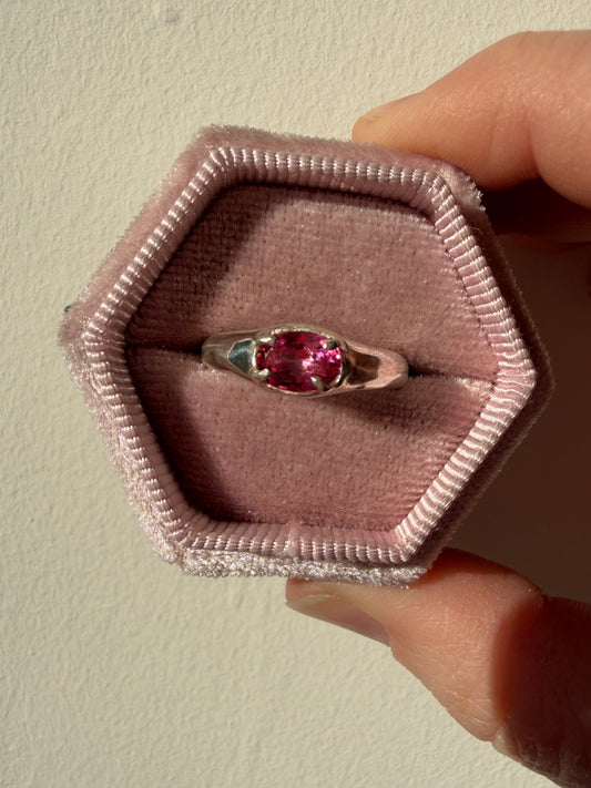 Silver ring with a pink gemstone in a hexagonal pink box held by a hand.