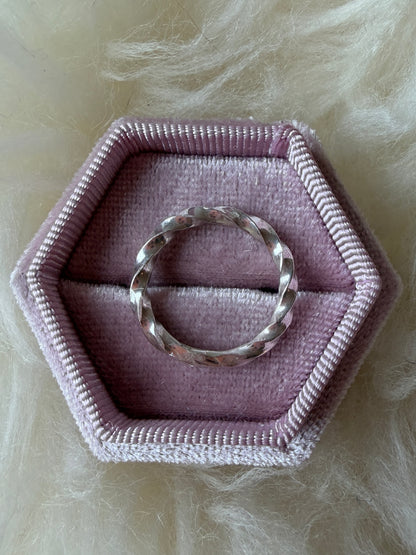 Sterling silver ring with continuous twists, pictured on its side, in a pink ring box against a white fur background.