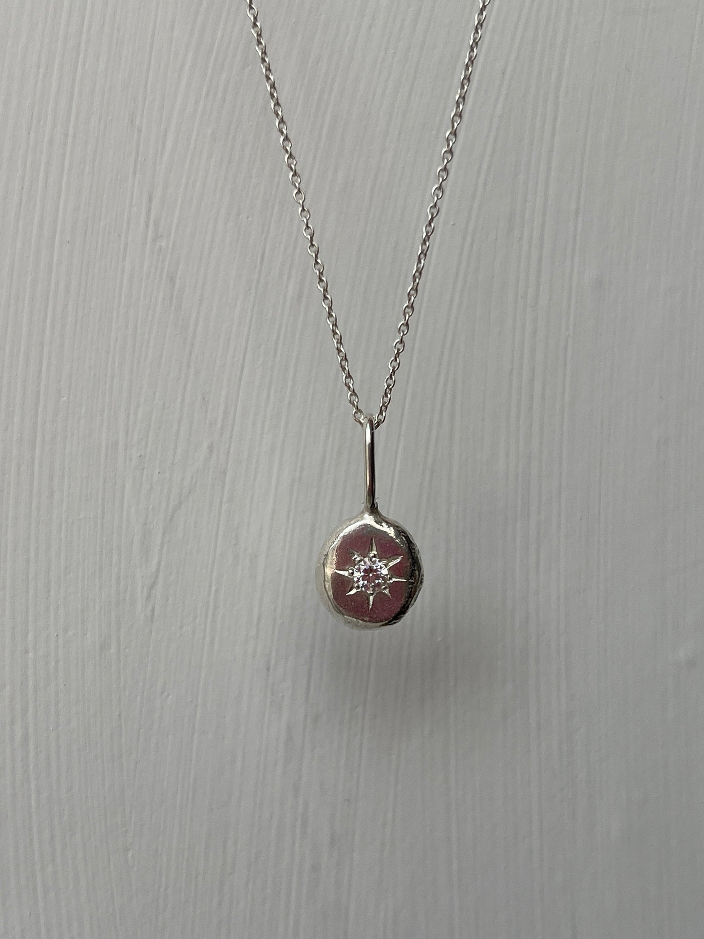 a sterling silver pendant with a star set cubic zirconia gemstone on a silver trace chain, pictured against a white background.