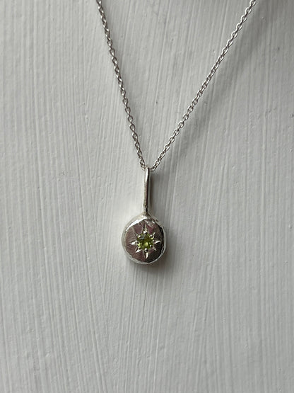 a sterling silver pendant with a star set peridot gemstone on a silver trace chain, pictured against a white background.