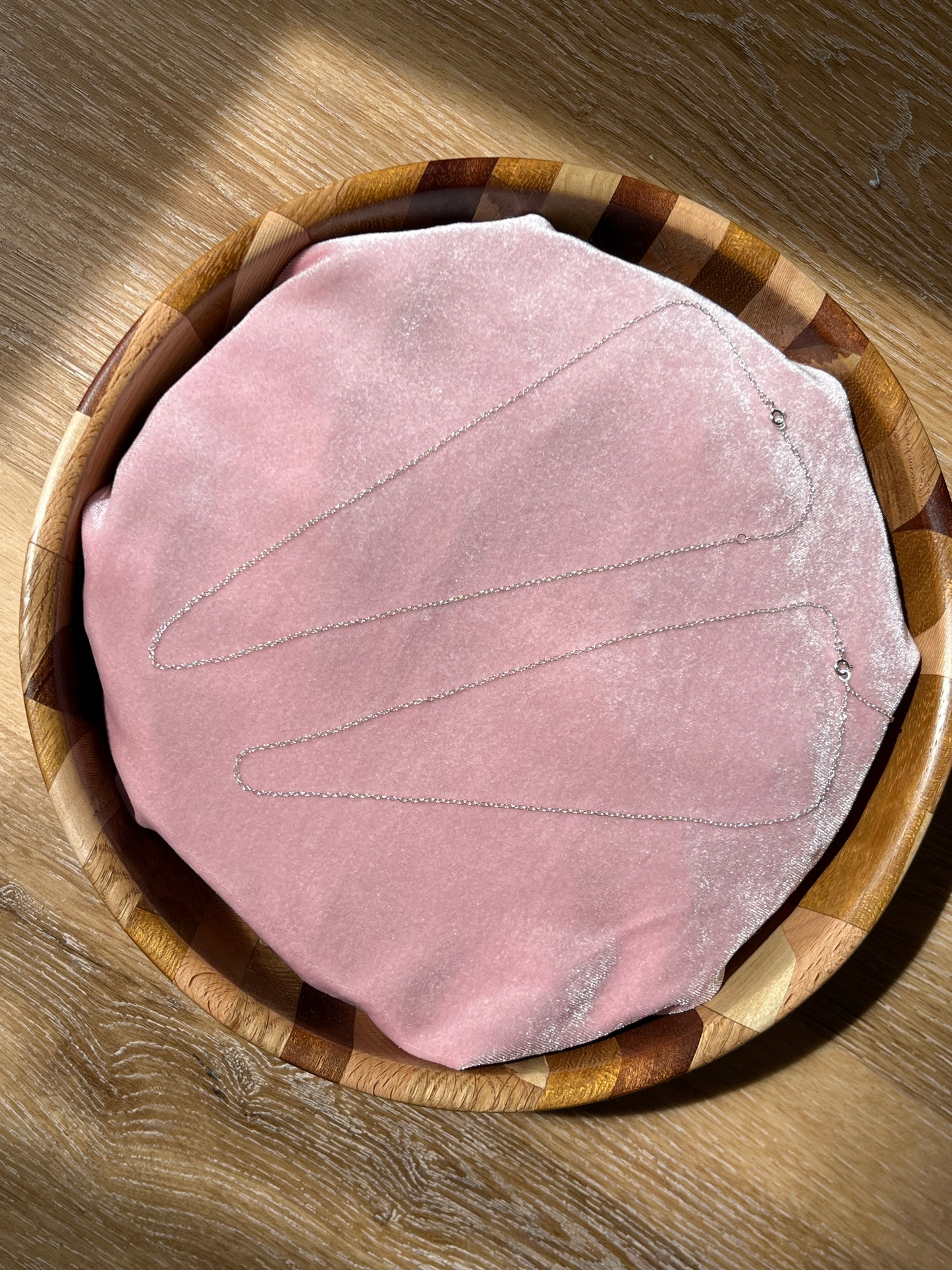 A sterling silver trace chain necklace laid out on a pink velvet and wooden surface