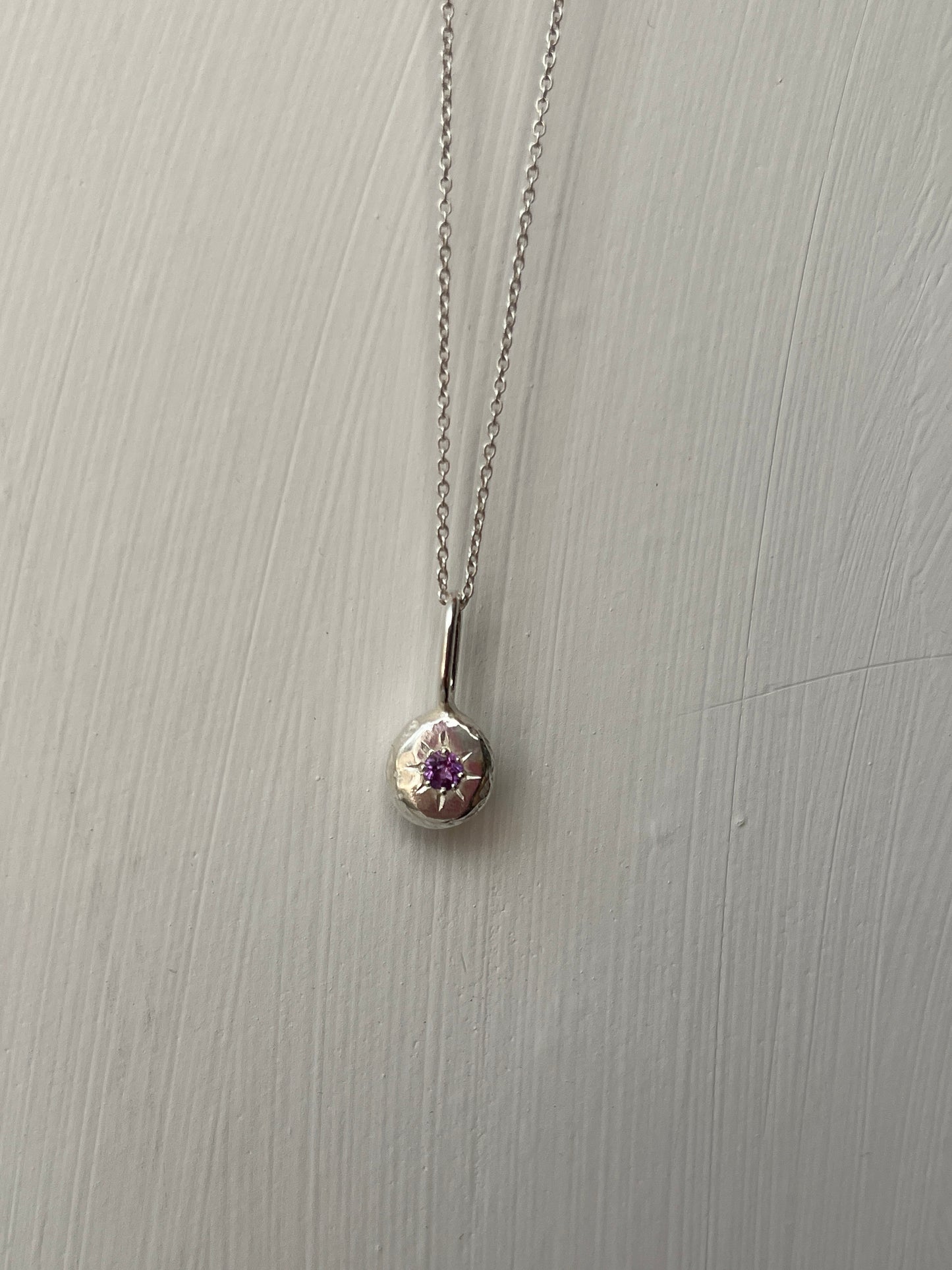 a sterling silver pendant with a star set purple amethyst gemstone on a silver trace chain, pictured against a white background.