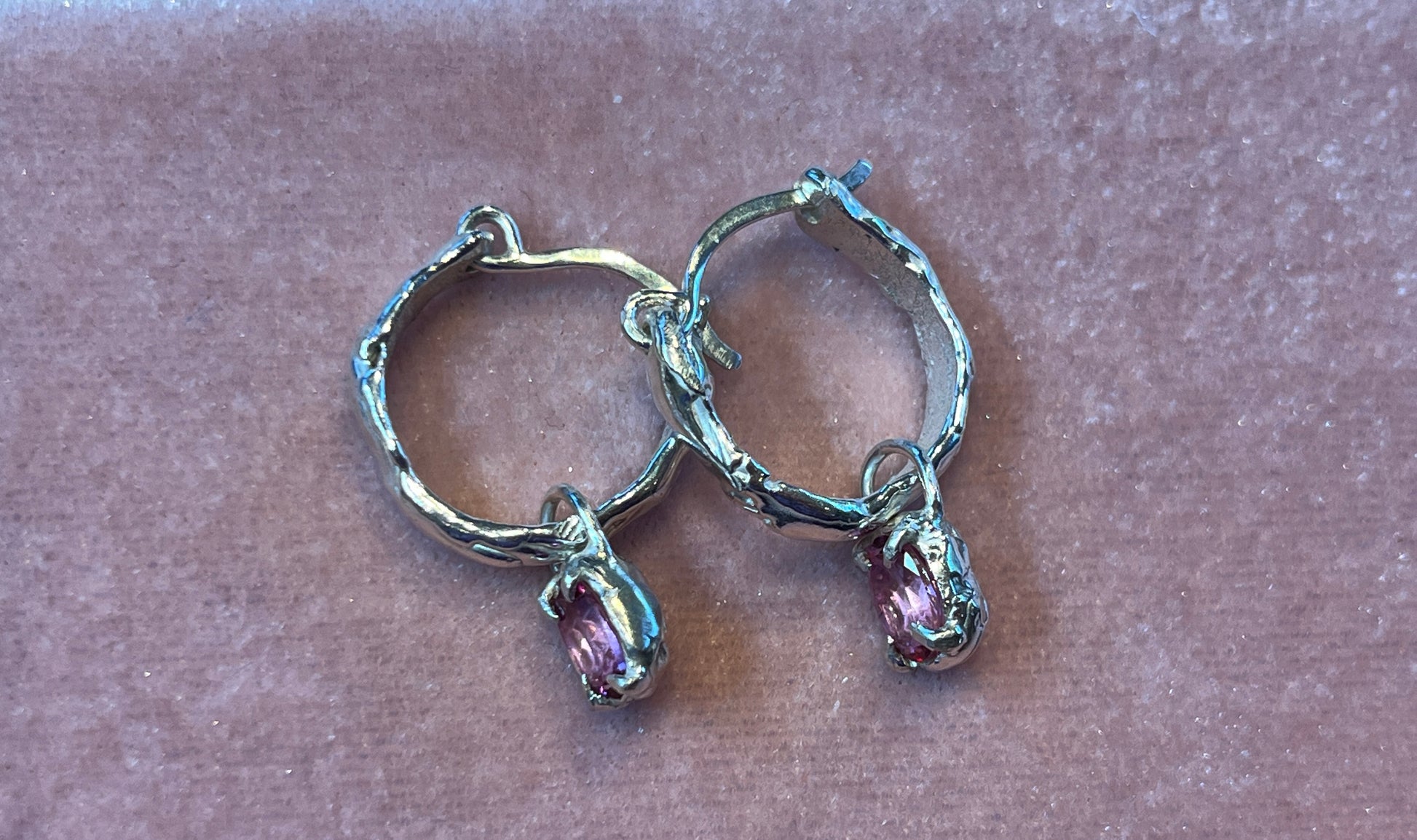 Silver hoop earrings with pink gemstones on a pale pink surface