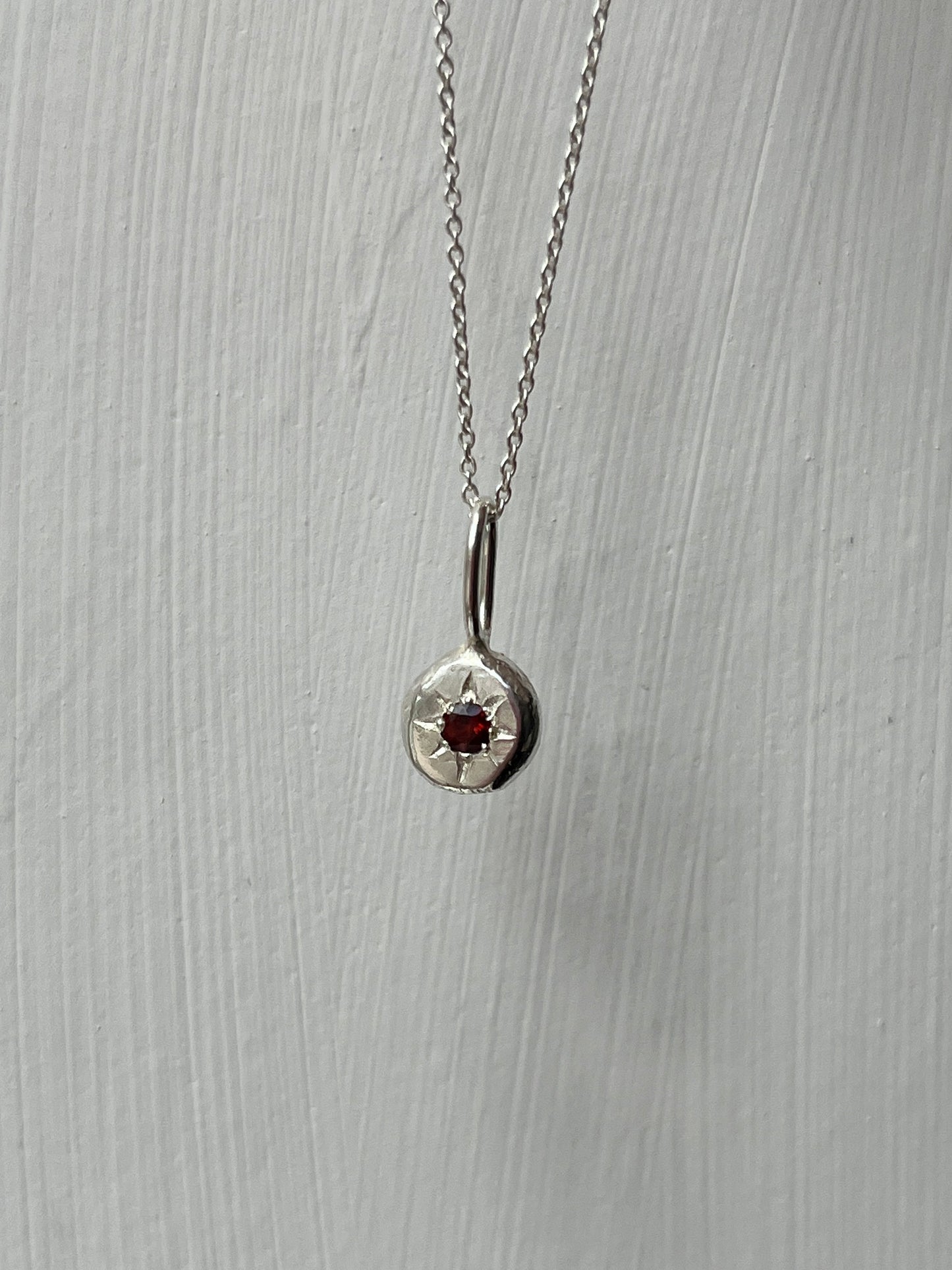 a sterling silver pendant with a star set a red garnet gemstone on a silver trace chain, pictured against a white background