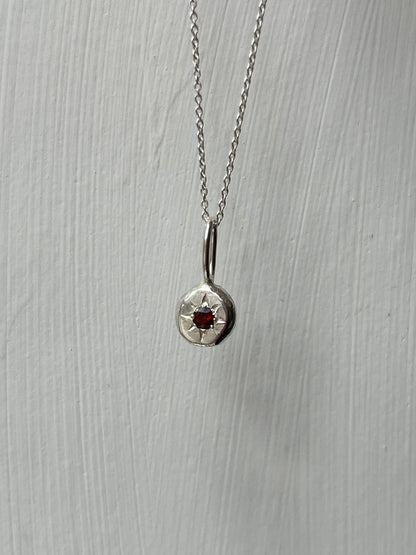 a sterling silver pendant with a star set a red garnet gemstone on a silver trace chain, pictured against a white background