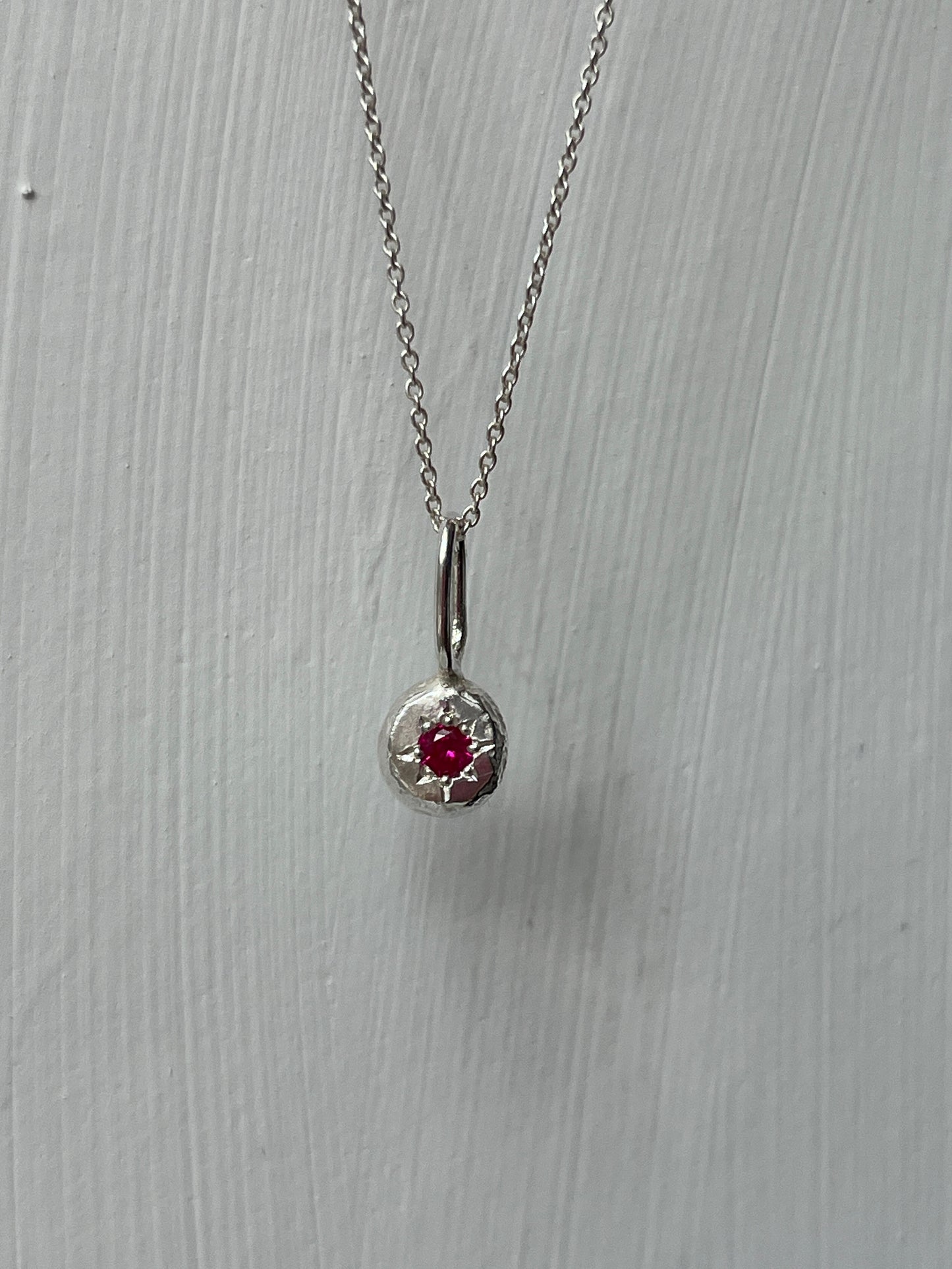 a sterling silver pendant with a star set ruby gemstone on a silver trace chain, pictured against a white background.