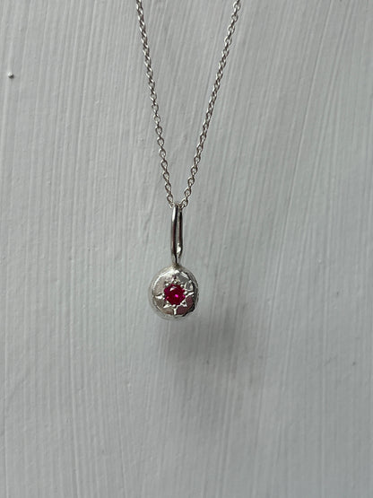 a sterling silver pendant with a star set ruby gemstone on a silver trace chain, pictured against a white background.