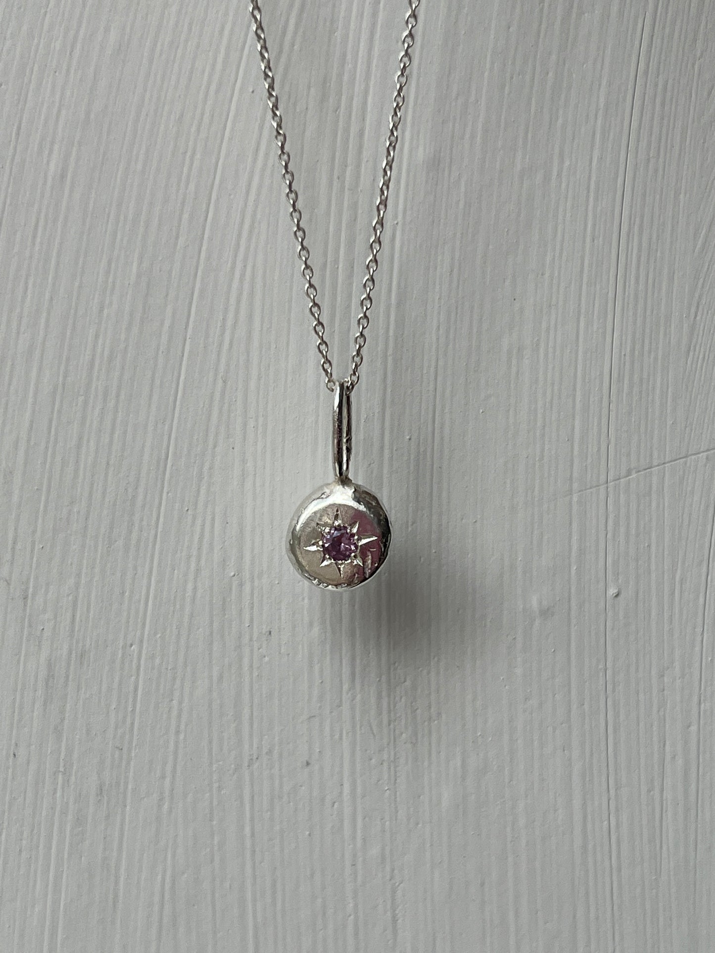 a sterling silver pendant with a star set alexandrite gemstone on a silver trace chain, pictured against a white background.