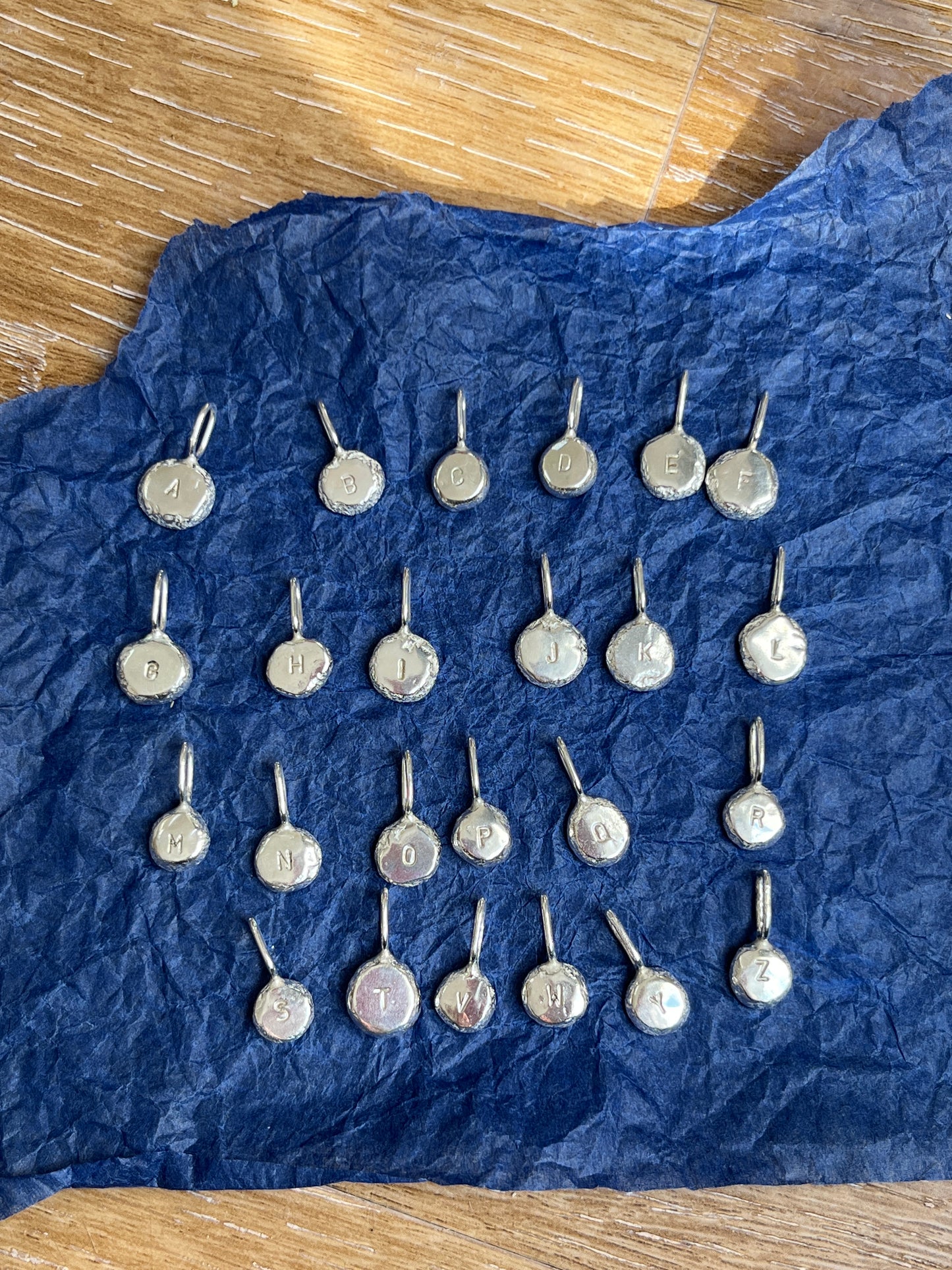 Silver letter pendants arranged alphabetically against a blur and wooden background.