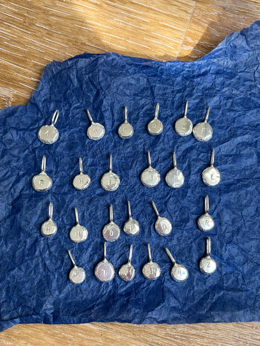 Silver letter pendants arranged alphabetically against a blur and wooden background.