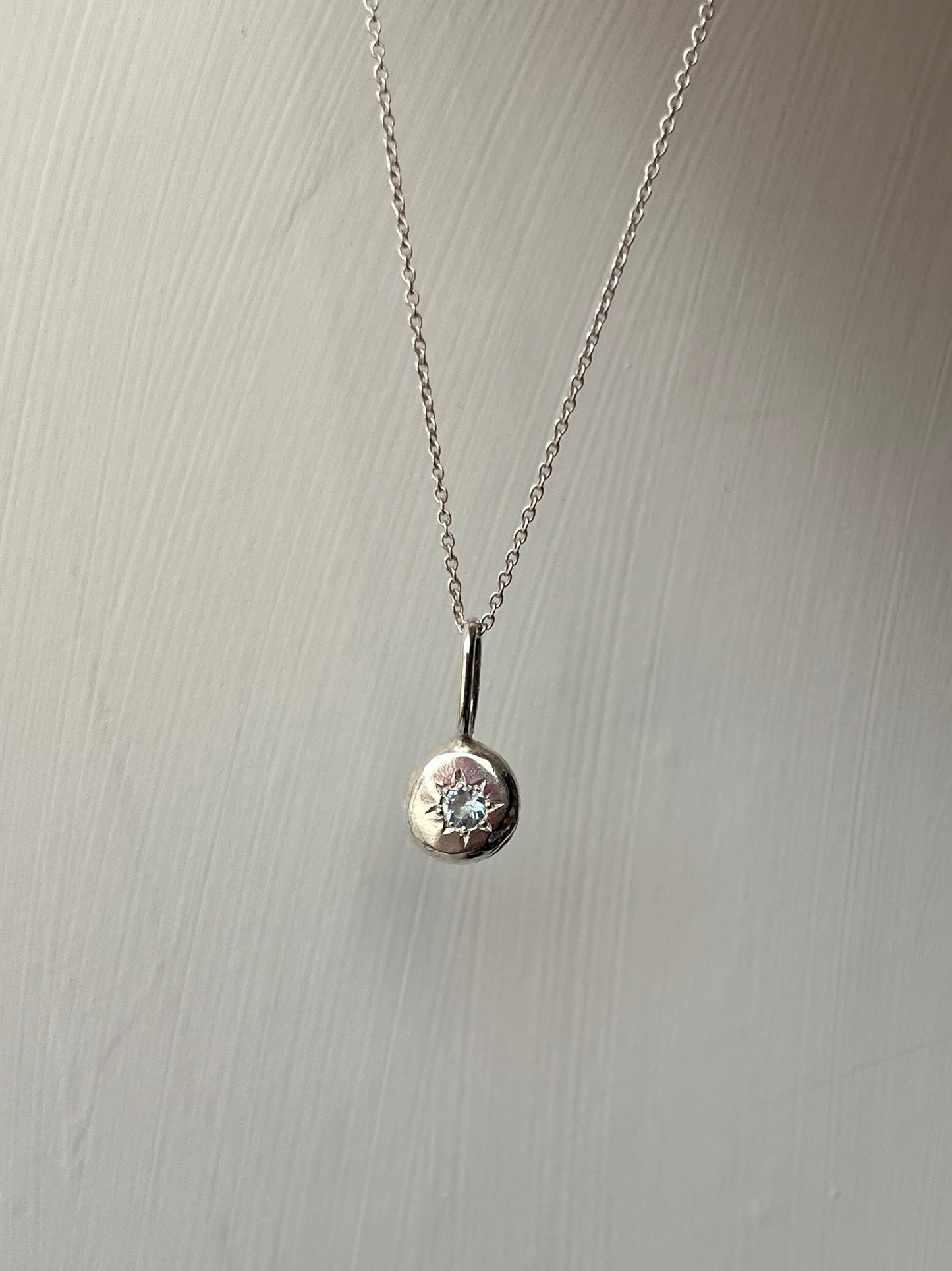 a sterling silver pendant with a star set aqaumarine gemstone on a silver trace chain, pictured against a white background.
