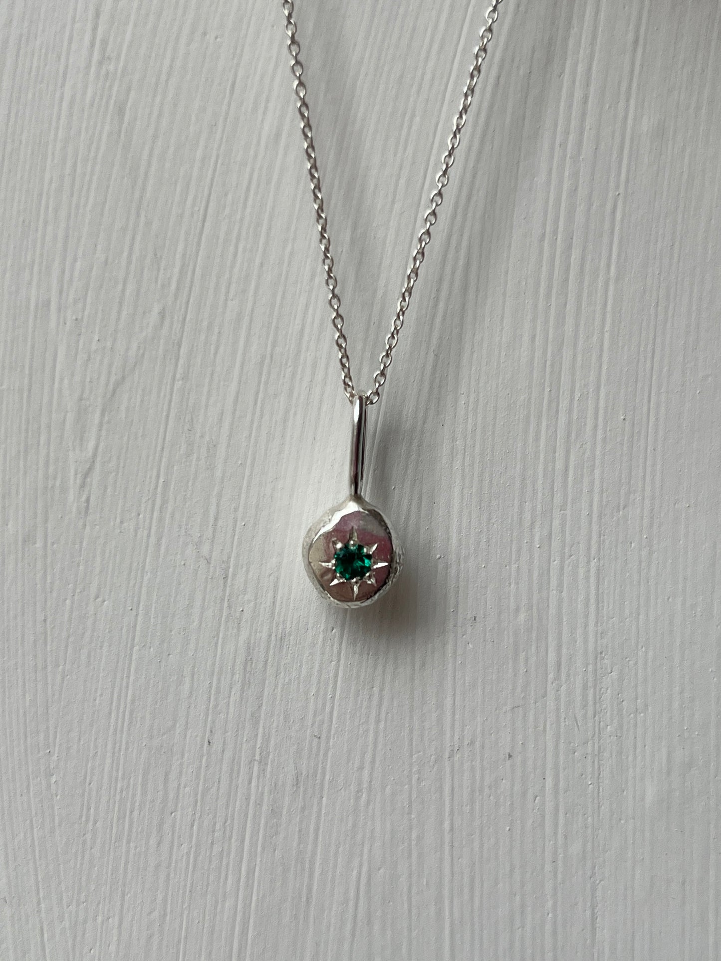 a sterling silver pendant with a star set emerald gemstone on a silver trace chain, pictured against a white background.