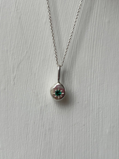a sterling silver pendant with a star set emerald gemstone on a silver trace chain, pictured against a white background.