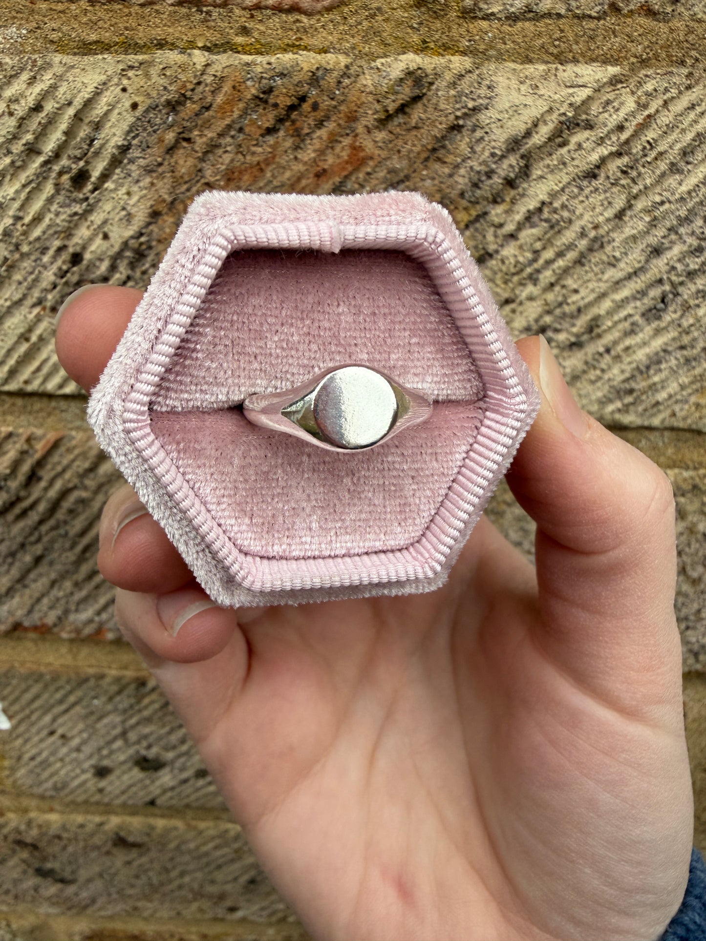 The silver mini signet pictured in a pink ring box with a brick background