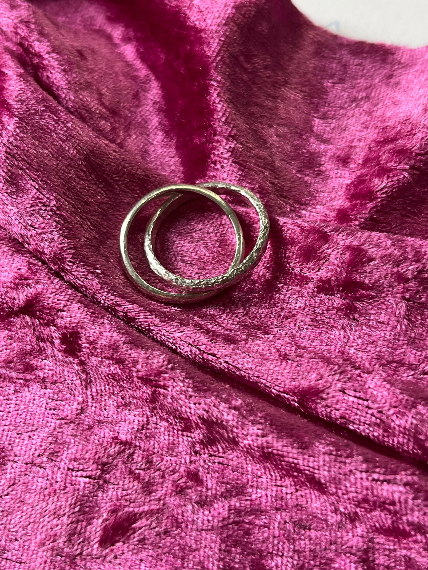 the sterling silver interlocked bands pictured flat against pink velvet. one band has smooth texture, the other has a rough texture resembling the surface of the moon.