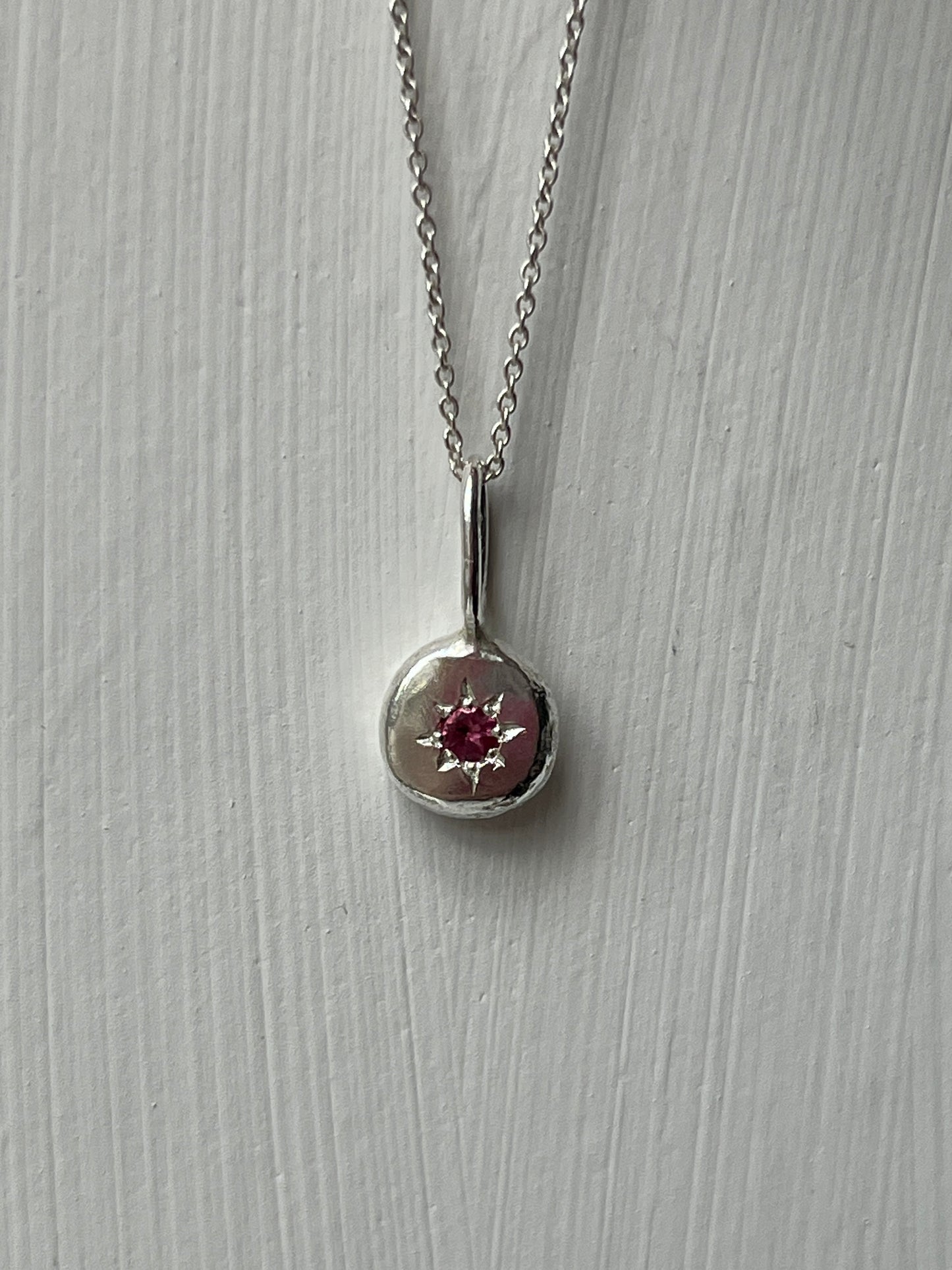a sterling silver pendant with a star set pink tourmaline gemstone on a silver trace chain, pictured against a white background.