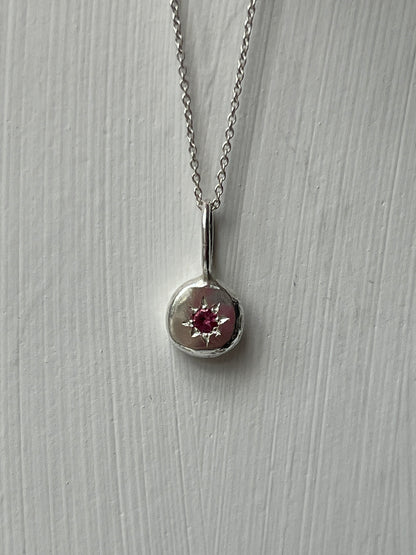 a sterling silver pendant with a star set pink tourmaline gemstone on a silver trace chain, pictured against a white background.