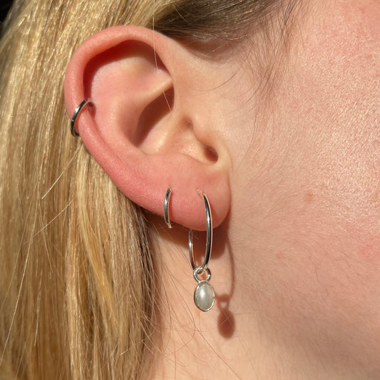 pearl droplet earring with sterling silver bezel on a sterling silver hoop 20mm wide. pictured modelled in ear.