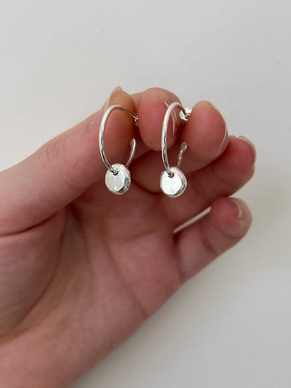 Silver hoop earrings held in a hand against a plain background